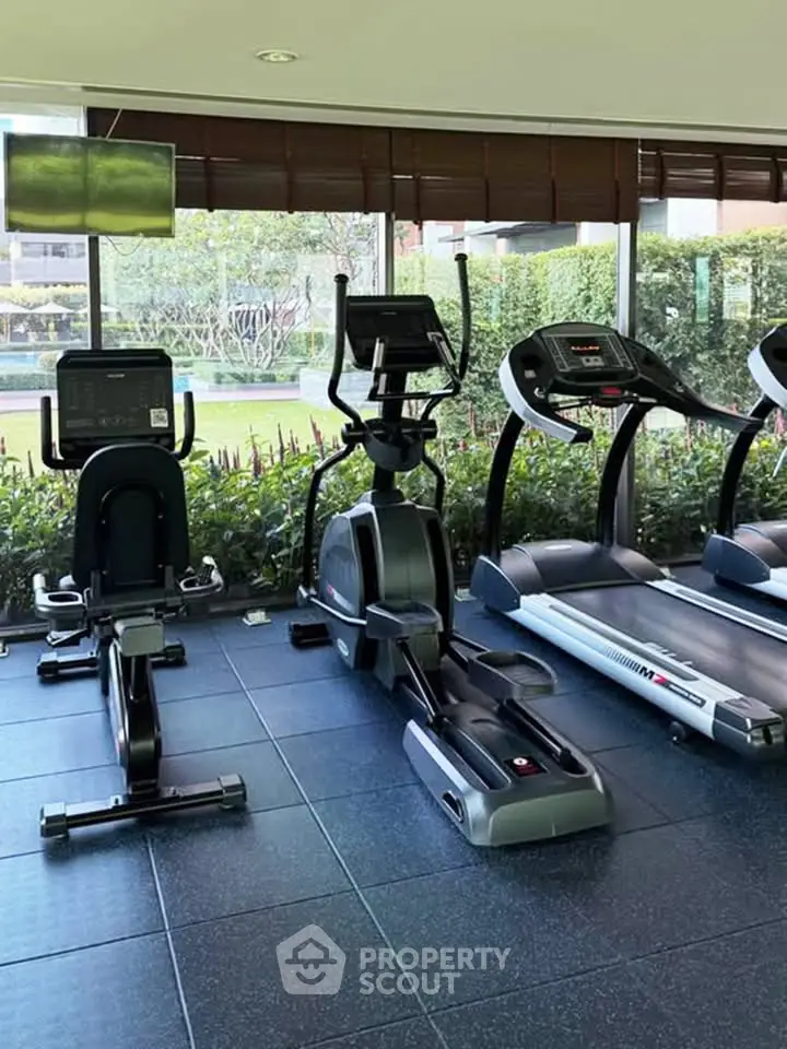 Modern gym with cardio equipment and garden view in luxury residential complex.
