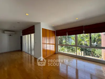 Spacious living room with large windows and wooden flooring, offering a serene garden view.