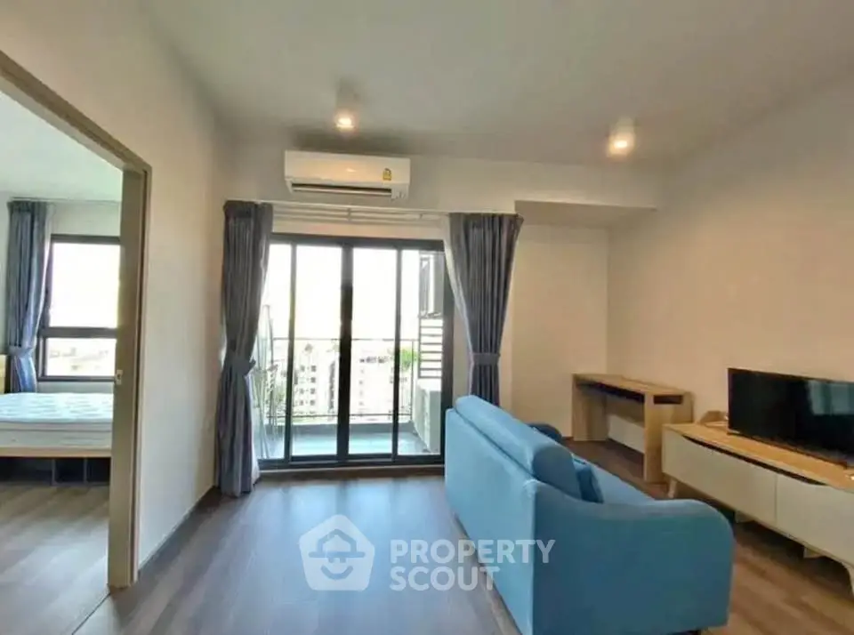 Modern living room with balcony view, blue sofa, and sleek TV setup in a bright apartment.