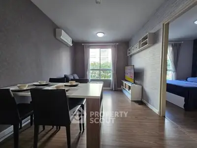 Modern living room with dining area and view into bedroom, featuring sleek furniture and natural light.