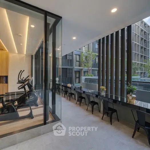 Modern gym with glass walls and outdoor seating area in luxury apartment complex.
