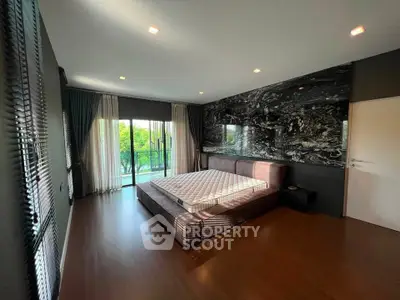 Spacious bedroom with modern decor and large windows opening to a lush green view.