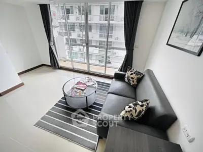 Modern living room with sleek sofa, glass coffee table, and large windows offering city view.