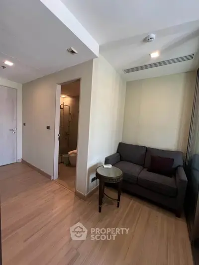 Cozy living room with wooden flooring and compact seating area, adjacent to a small bathroom.