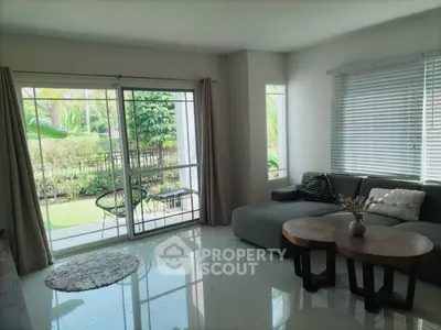 Spacious living room with large windows and garden view, featuring modern furniture and natural light.