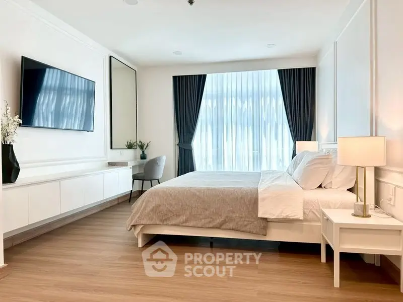 Elegant bedroom with modern decor, large window, and wall-mounted TV in a stylish apartment.