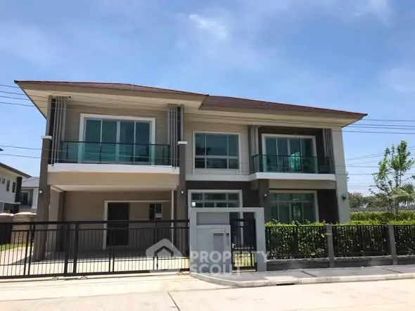 Modern two-story house with large windows and gated entrance in a suburban neighborhood.