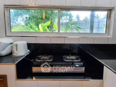 Modern kitchen with gas stove and appliances, featuring a scenic garden view through the window.