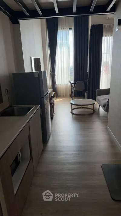 Modern apartment interior with open kitchen and cozy living area, featuring large windows and stylish decor.