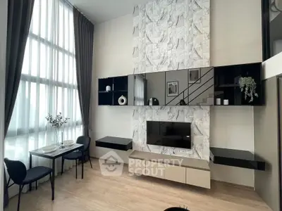 Modern living room with high ceilings and stylish decor, featuring a marble accent wall and large windows.