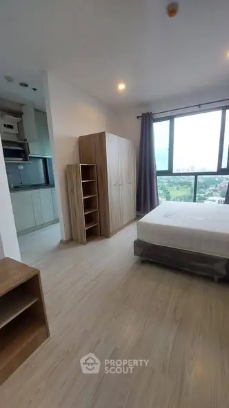 Modern bedroom with large window and adjacent kitchen area, featuring sleek wooden furniture.