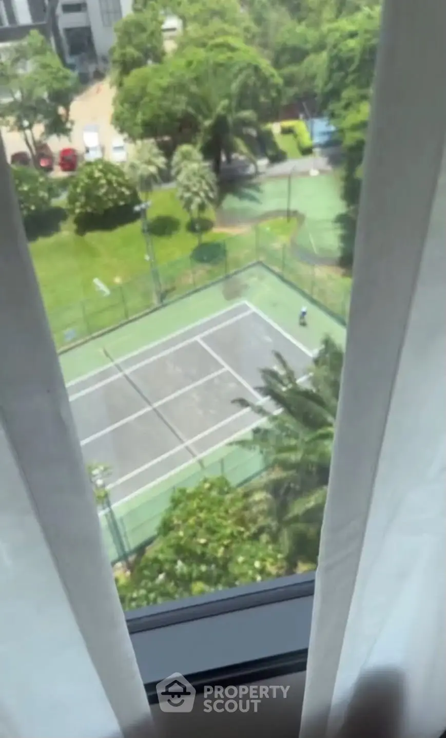 Stunning view of tennis court from window, lush greenery surrounds the area, perfect for sports enthusiasts.
