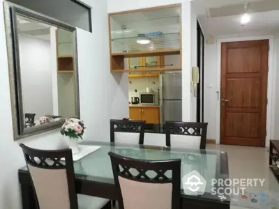 Charming dining area with glass table and elegant chairs adjacent to a compact kitchen.