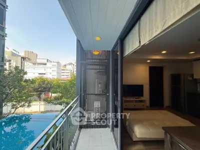 Modern apartment with balcony overlooking pool and city view, featuring open living space and sleek kitchen.