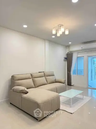 Modern living room with beige sofa, sleek lighting, and large window for natural light.