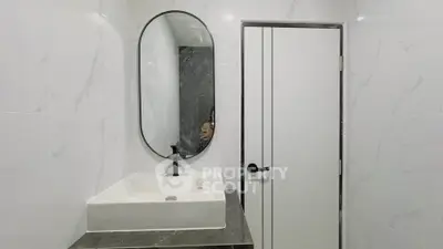 Modern bathroom with sleek sink and oval mirror, featuring elegant marble walls.