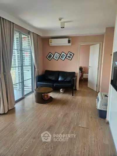 Modern living room with wooden flooring, black sofa, and balcony access in a stylish apartment.