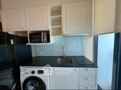 Modern kitchen with sleek appliances and ample storage space, featuring a washing machine and microwave.