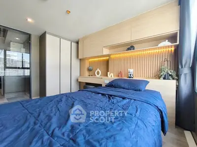 Modern bedroom with blue bedding, built-in wooden storage, and ambient lighting.