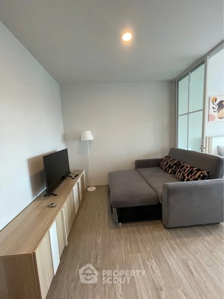 Modern living room with sleek gray sofa, stylish TV stand, and elegant floor lamp in a cozy apartment.