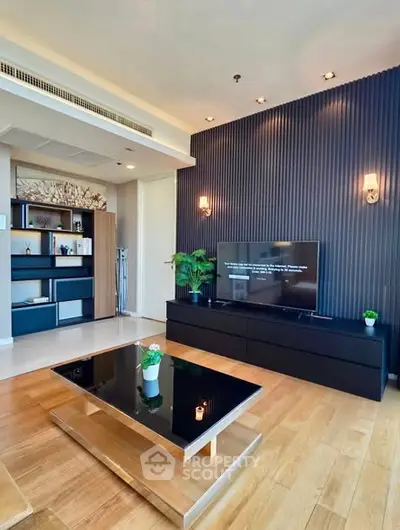 Modern living room with sleek black furniture and wooden flooring, featuring a stylish TV setup and decorative plants.