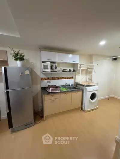 Modern kitchen with fridge, washing machine, and open shelving in compact layout.