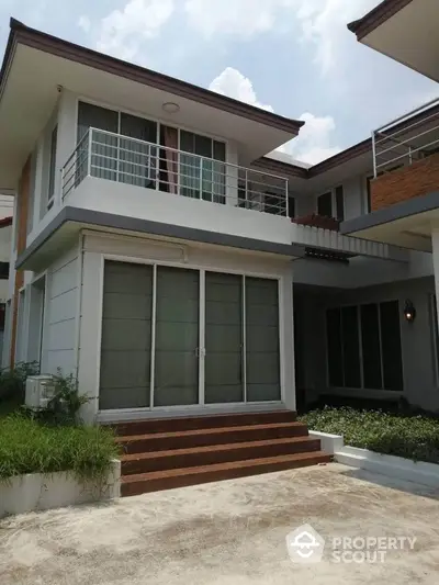 Modern two-story house with large windows and balcony in a serene neighborhood.