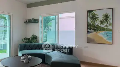 Stylish living room with curved sofa and beach-themed artwork, offering a serene view of the garden.