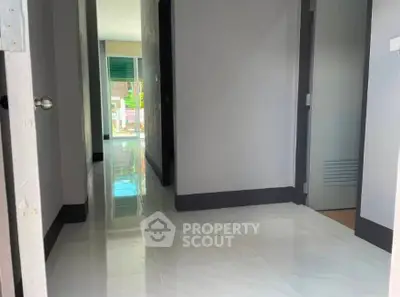 Modern hallway with glossy floors leading to a bright room with large windows.