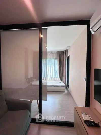 Modern apartment with sliding glass door separating living room and bedroom, featuring sleek design and natural light.