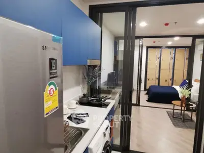 Modern apartment kitchen with sleek appliances and view into cozy bedroom