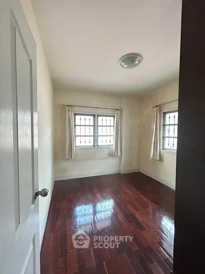 Spacious empty room with wooden floors and large windows, perfect for customization.