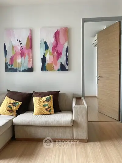 Modern living room with stylish sofa and abstract art, featuring wooden flooring and open door to another room.