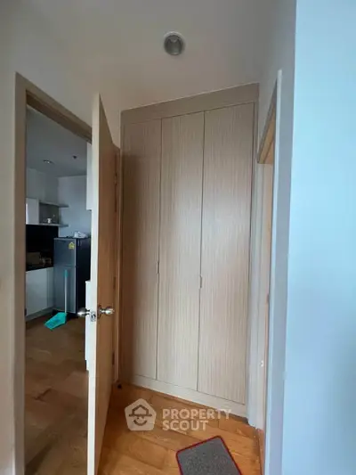 Modern apartment interior with wooden flooring and built-in storage closet near kitchen area.