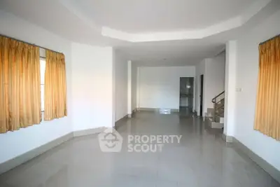 Spacious empty living room with tiled flooring and large windows with curtains.