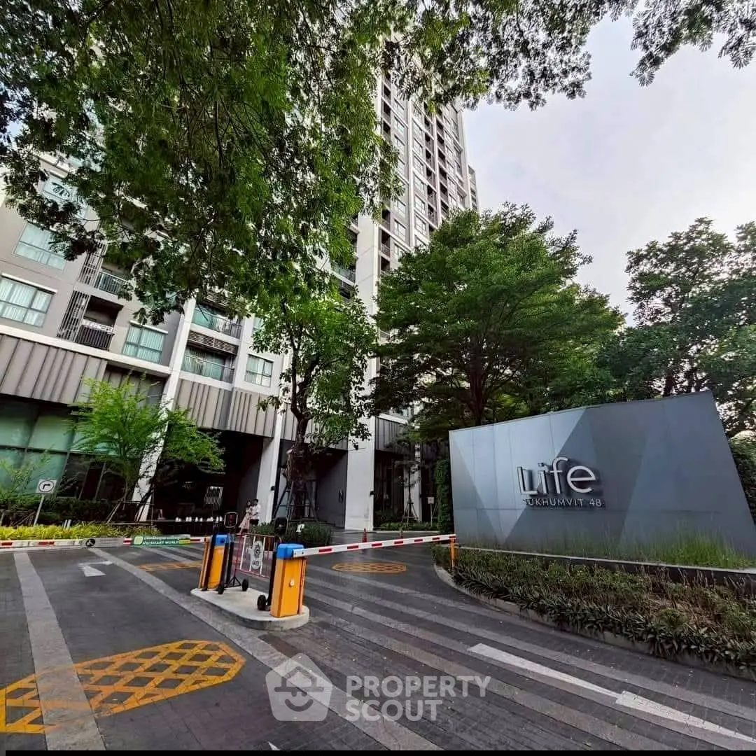 Modern high-rise condominium entrance with lush greenery and secure access in urban setting.