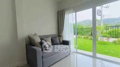 Modern living room with gray sofa and large glass doors opening to a lush garden view.