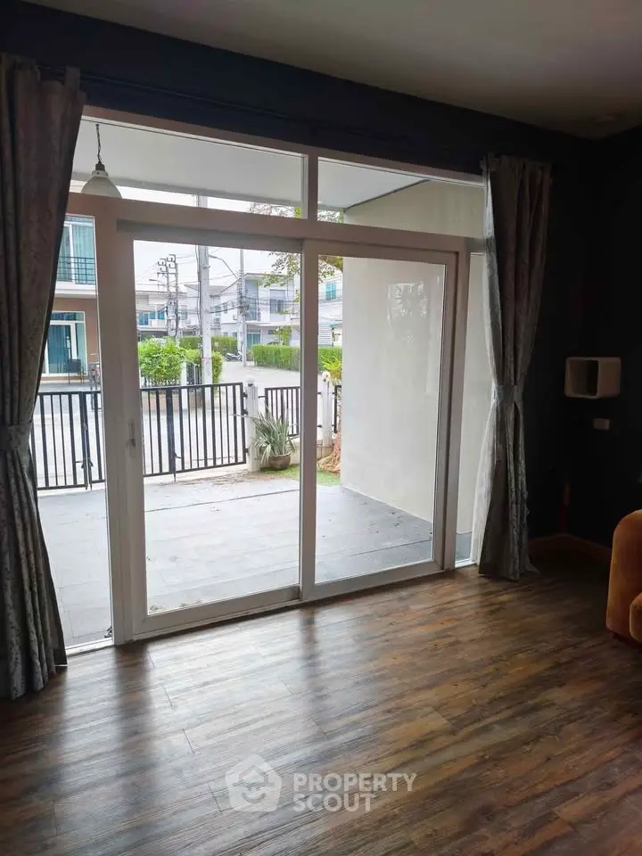 Spacious living room with sliding glass doors leading to a balcony, featuring elegant curtains and wooden flooring.