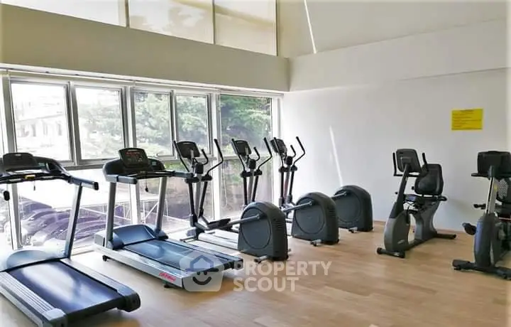 Spacious gym with modern exercise equipment and large windows for natural light.