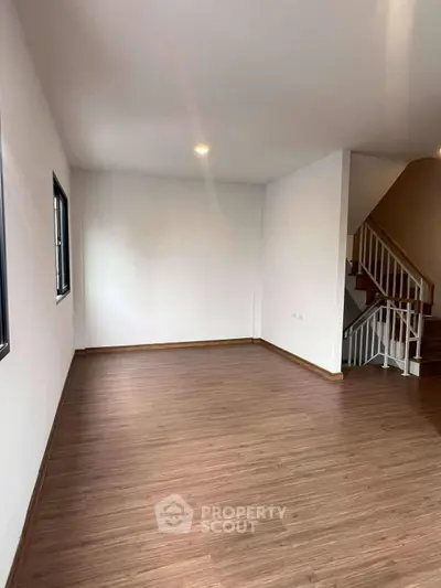 Spacious empty room with wooden flooring and staircase, ideal for customization.