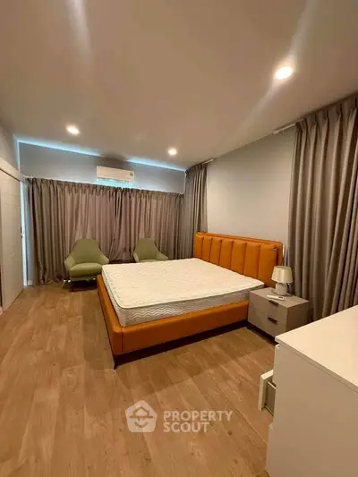 Spacious bedroom with modern decor and wooden flooring, featuring a comfortable bed and stylish seating area.
