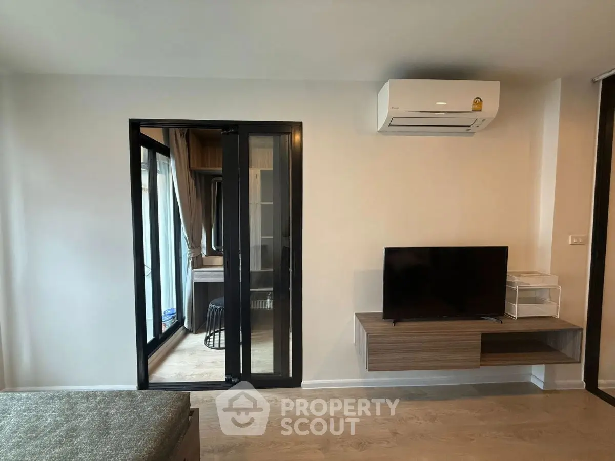 Modern living room with air conditioning and TV, featuring a sliding glass door to a cozy balcony.