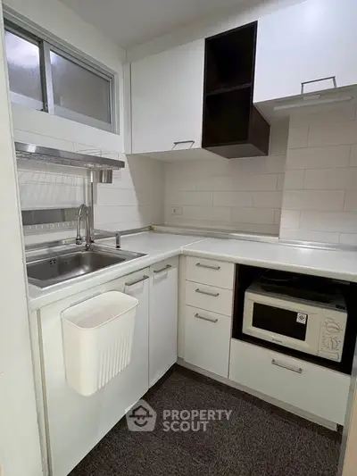 Modern compact kitchen with sleek white cabinets and built-in microwave, perfect for efficient cooking.
