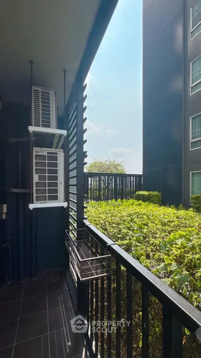 Modern apartment balcony with lush greenery view and air conditioning units.