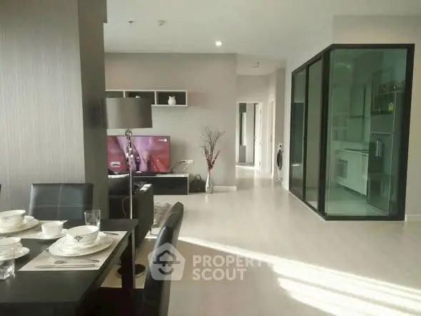 Modern open-plan living room with sleek dining area and glass-enclosed kitchen