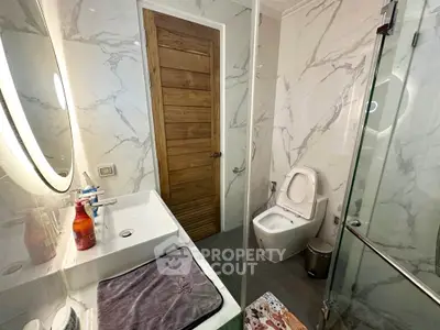 Modern bathroom with marble walls, glass shower, and wooden door for a luxurious touch.