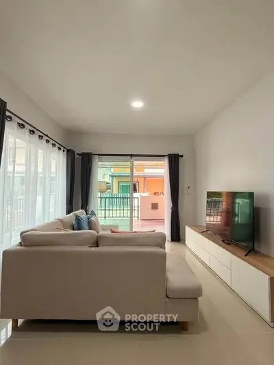 Spacious living room with modern sofa and large TV, featuring natural light and balcony access.