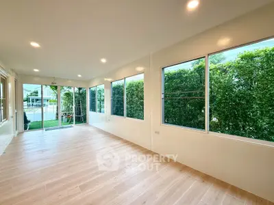 Spacious sunlit room with large windows and garden view, perfect for relaxation.