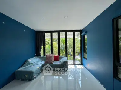 Modern living room with blue walls and large windows overlooking a lush garden.