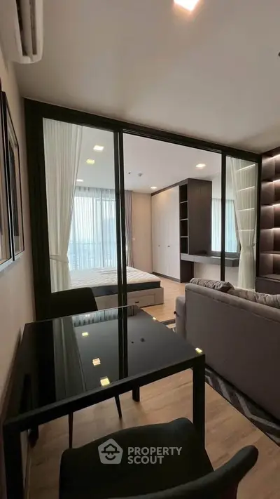 Modern studio apartment with glass partition, sleek furniture, and ample natural light.